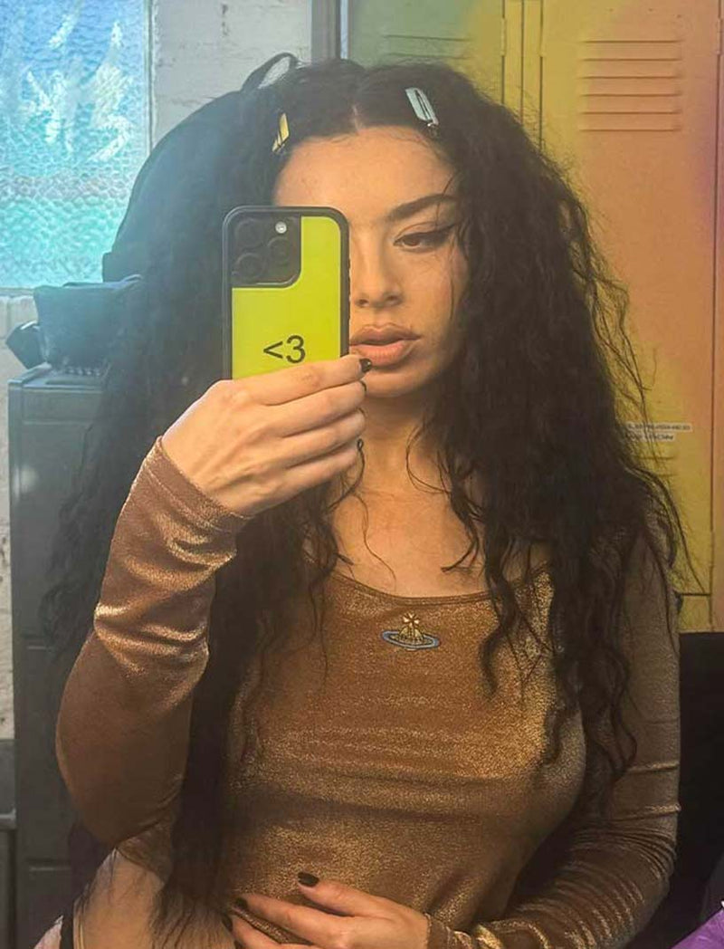 Charli XCX takes a mirror selfie with her Wf case, bright green with an emoticon heart in the middle