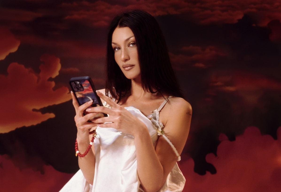 Bella Hadid poses in a silk white dress, holding her Orebella x WF phone case