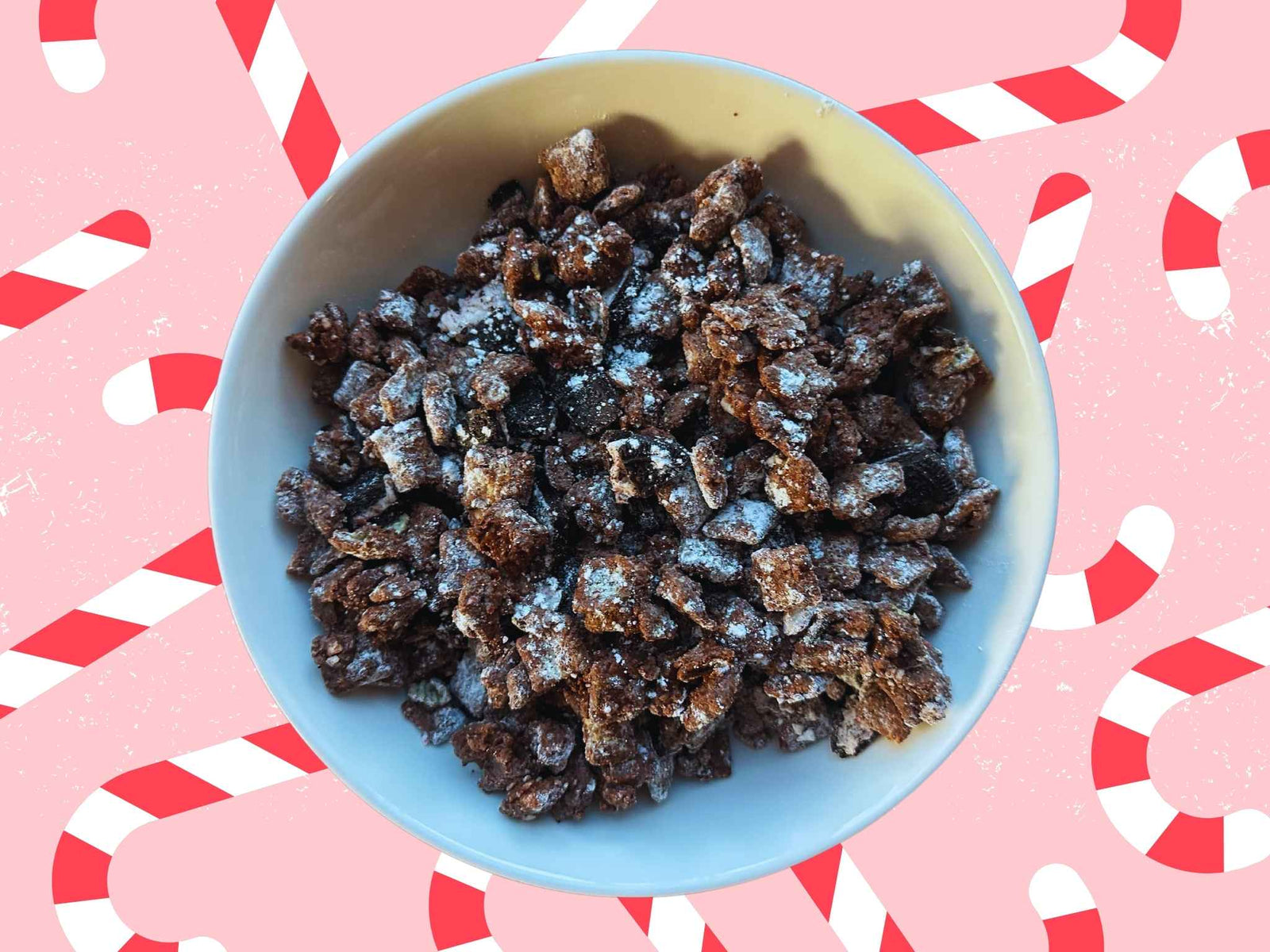 A bowl of muddy buddies in a white bowl sits on a background of candy canes