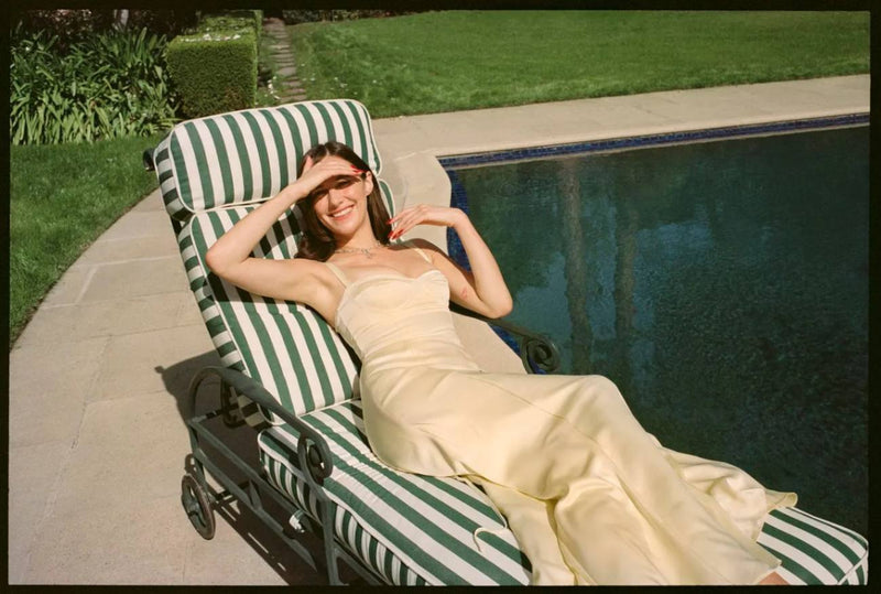 Devon Lee lays on a striped beach chair in a butter yellow dress