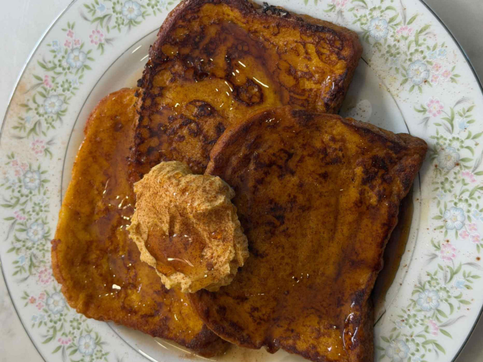 A close up of french toast with syrup and butter are placed on a floral white plate