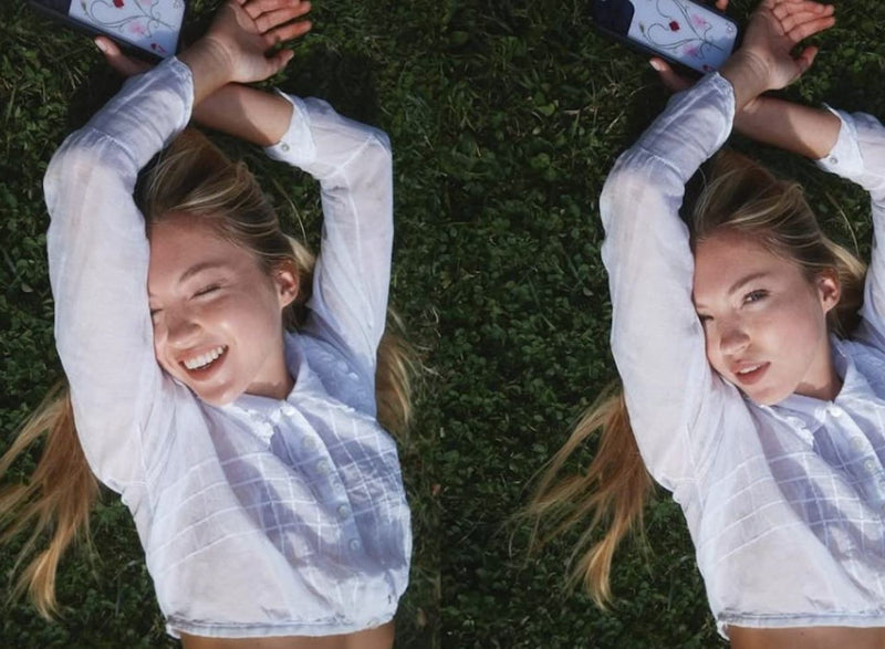 Lila Moss lays on the grass with her arms up in a white long sleeve