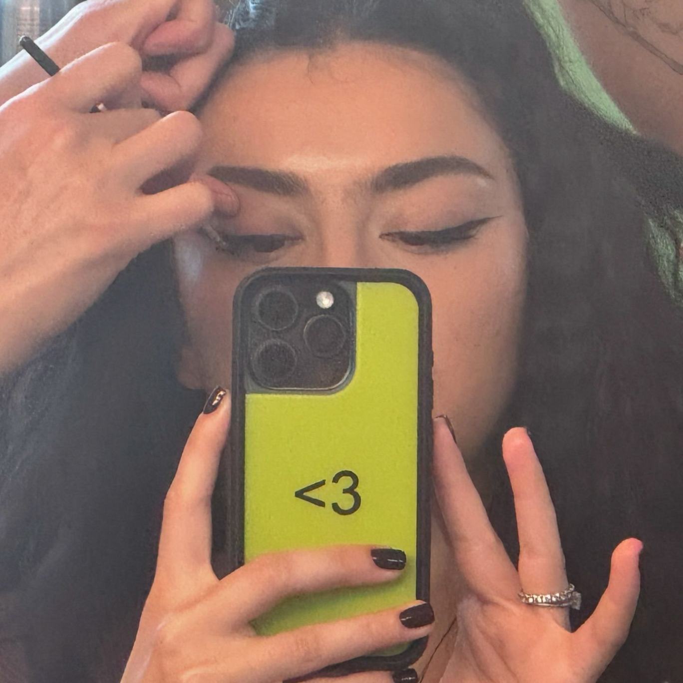 Charli XCX takes mirror selfie with her custom green BRAT wildflower case with a black emoticon heart in the middle