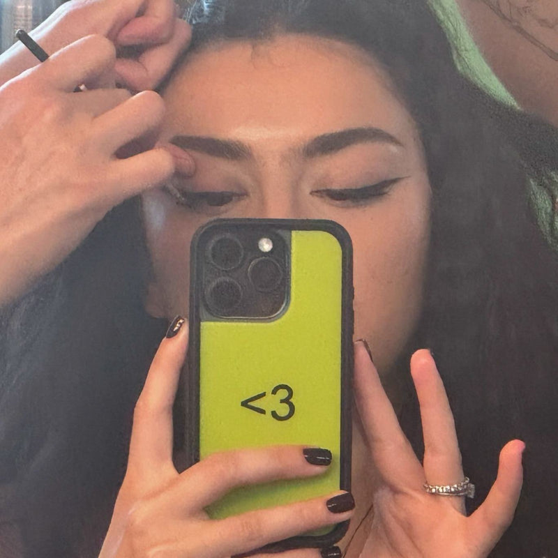 Charli XCX takes mirror selfie with her custom green BRAT wildflower case with a black emoticon heart in the middle