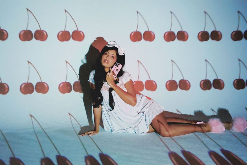 Cindy Kimberly poses in front of a cherry background as she lays on ground