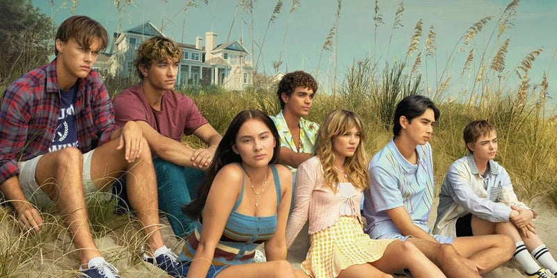 Cast of the Summer I Turned Pretty sit in a field in the sand
