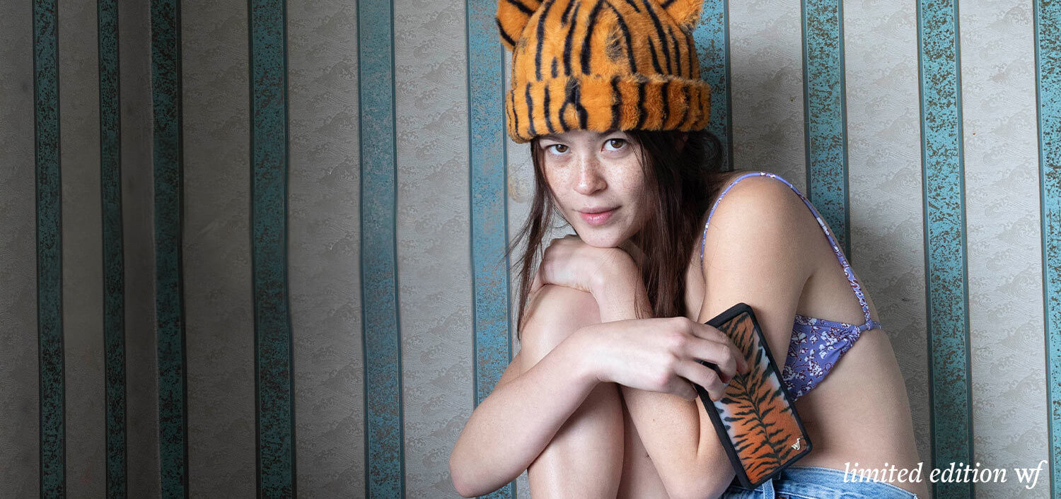Person wearing a tiger-striped hat and holding a phone against a striped wall.